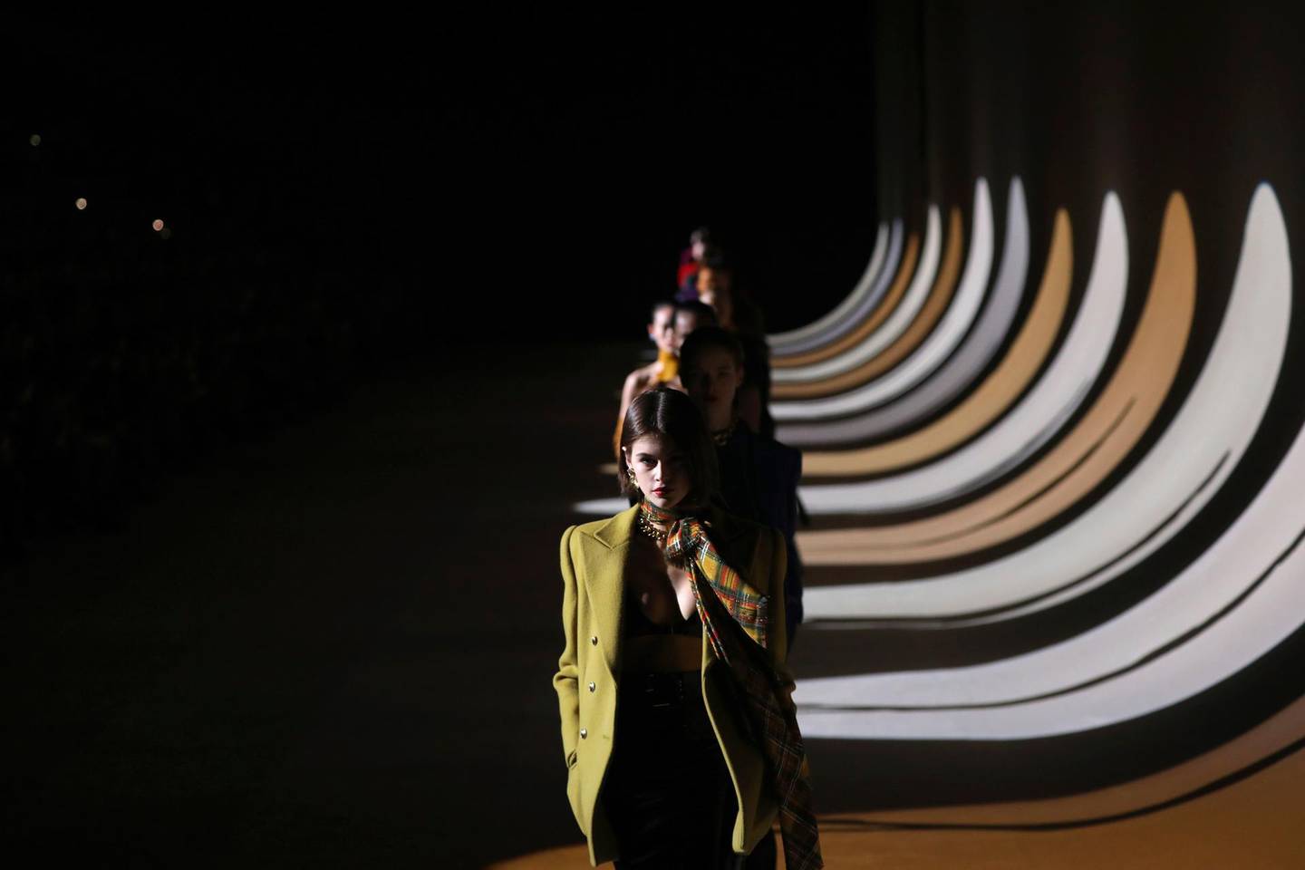 FILE - In this Feb.25, 2020 file photo, model Kaia Gerber leads other models as they wear creations for the Saint Laurent fashion collection during Women's fashion week Fall/Winter 2020/21 presented in Paris. Gucci and St. Laurent are two of the highest profile fashion houses to announce they will leave the fashion calendar behind, with its relentless four-times a year rhythm, shuttling cadres of fashionistas to global capitals where they squeeze shoulder-to-shoulder around runways for 15 breathless minutes. The coronavirus lockdown -- which has hit luxury fashion houses on their bottom lines -- has also given pause to rethink the pace of fashion. (Photo by Vianney Le Caer/Invision/AP, File)