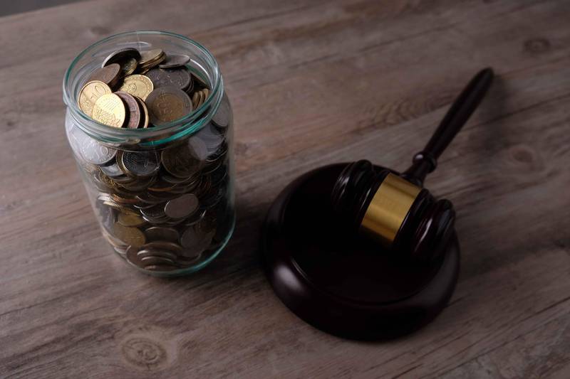 High Angle View Of Coins In Glass Of Jar On Table With Gavel. Getty Images