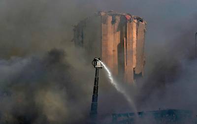 Firefighters stand on a ladder amid billowing smoke as they extinguish the remaining flames at the seaport of Beirut. AFP