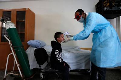 A Palestinian health worker wearing a protective facemask checks the body temperature of a child at a UNRWA school at Al Shati refugee camp in Gaza City. AFP