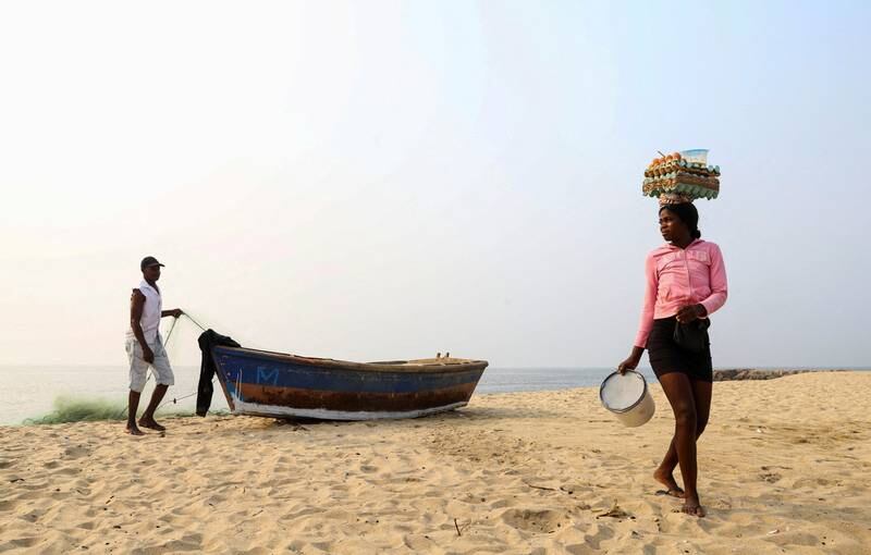 A woman selling eggs walks past a man preparing his boat, in Luanda, Angola. Reuters