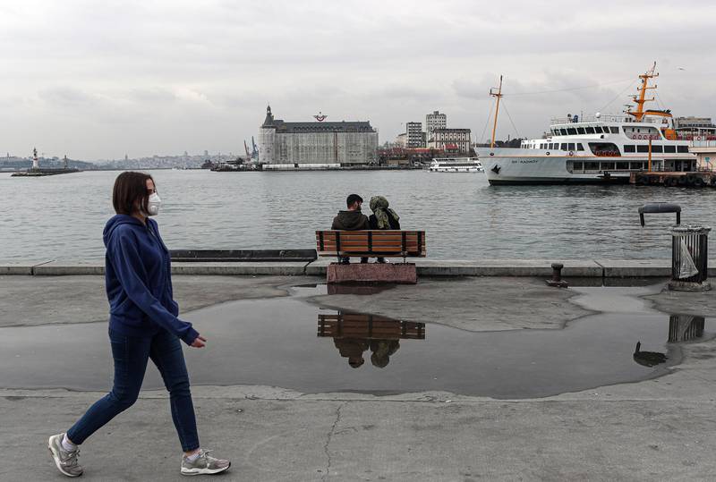 epa08341640 A woman wearing a protective face mask walks past a couple sitting at the Kadikoy harbour on the Bosphorus amid the ongoing coronavirus COVID-19 pandemic in Istanbul, Turkey, 03 April 2020. Turkey suspended all international flights and all inter-city travels are subject to local authorities' permission as part of measures to prevent the spread of the pandemic COVID-19 disease caused by the SARS-CoV-2 coronavirus. The country decided also to halt public events, temporarily shut down schools, and suspend sporting events.  EPA/SEDAT SUNA