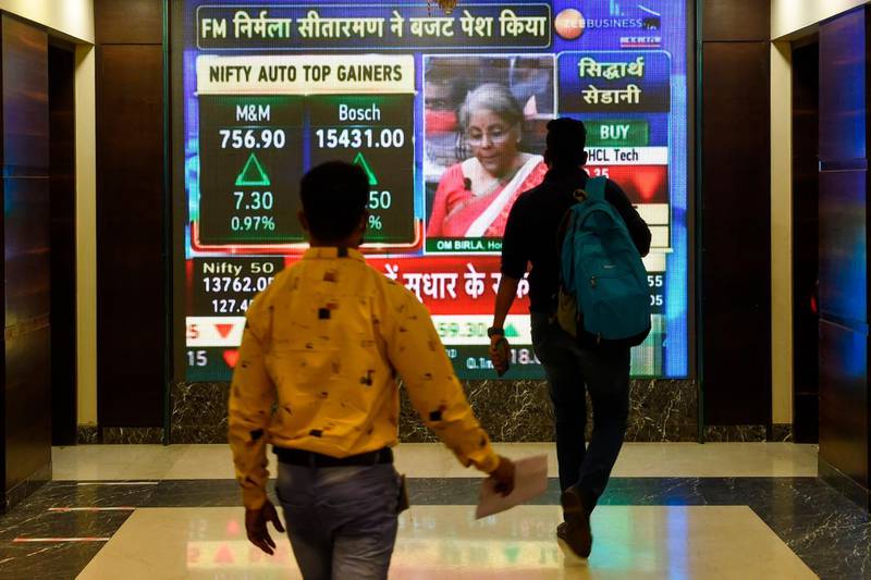Office workers walk past a digital screen showing Indian Finance Minister Nirmala Sitharaman delivering the budget speech in parliament, at the Bombay Stock Exchange (BSE) in Mumbai on February 1, 2021. / AFP / Punit PARANJPE
