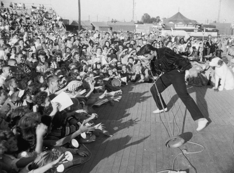 Elvis performs outdoors on a small stage to the adulation of a  young crowd in 1957