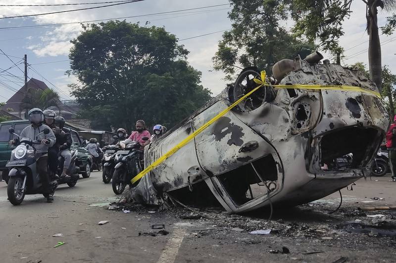 Motorists ride past the wreckage of a car burned outside Kanjuruhan Stadium. AP