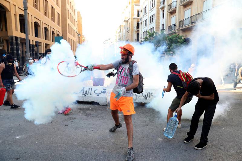 An anti-government protester uses a a tennis racket to hit back a tear gas canister towards at riot policemen during a protest following last Tuesday's massive explosion which devastated Beirut, Lebanon, Monday, Aug. 10, 2020. (AP Photo/Bilal Hussein)