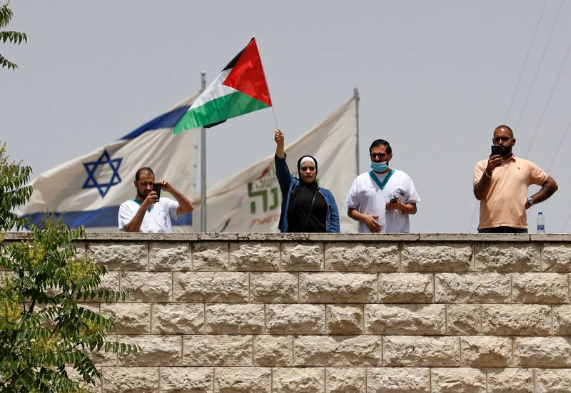 A Palestinian woman waves a national flag on the rooftop of a building where an Israeli flag has been placed, hours before the funeral in Jerusalem. AFP