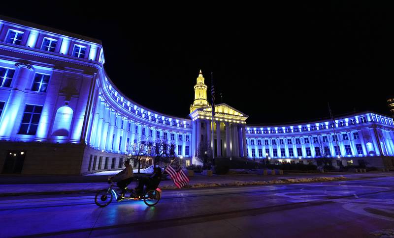 An American flag unfurls off a pedicab as it glides past the Denver City/County Building, which is illuminated in yellow and blue in support of Ukraine. AP
