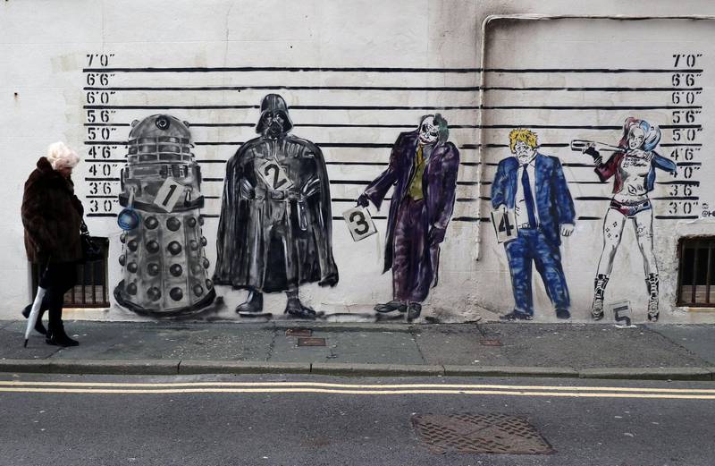 A woman walks past a graffiti mural that depicts Britain's Prime Minister Boris Johnson alongside fictional characters of a Dalek, Darth Vader, The Joker and Harley Quinn. Reuters