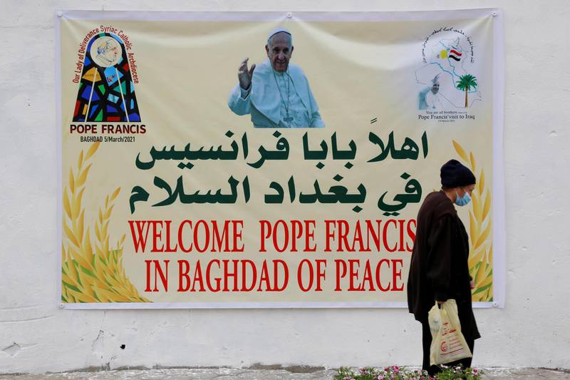 A woman walks near a poster of Pope Francis upon his upcoming visit to Iraq, in Baghdad, Iraq March 4, 2021. REUTERS/Teba Sadiq