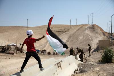 A Palestinian Bedouin boy waves a Palestinian flag in front of Israeli soldiers at al-Khan al-Ahmar near Jericho in the occupied West Bank July 4, 2018. REUTERS/Ronen Zvulun