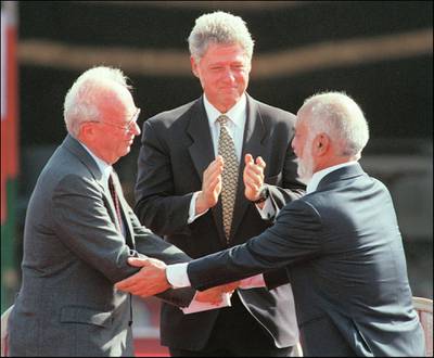 US President Bill Clinton (c) applauds as Jordan's King Hussein Ibn Talal (r) and Israeli Premier Yitzhak Rabin shake hands during the Israeli-Jordanian Peace Treaty signing ceremony at the Araba Israeli-Jordanian border 26 October 1994. (Photo by SVEN NACKSTRAND / AFP FILES / AFP)