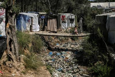 A woman with a child cross a wooden bridge in a improvised tents camp near the refugee camp of Moria in the island of Lesbos on June 21, 2020. - Greece's announcement that it was extending the coronavirus lockdown at its migrant camps until July 5, cancelling plans to lift the measures on June 22, coincided with World Refugee Day on June 27, 2020. (Photo by ARIS MESSINIS / AFP)