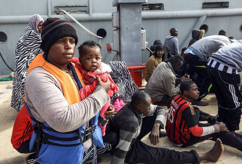 An African migrant carries a child while walking on a dock at the Libyan capital Tripoli's naval base on March 10, 2018, after disembarking following rescue from off the coast of Zawiyah, about 45 kilometres west of the capital. / AFP PHOTO / MAHMUD TURKIA