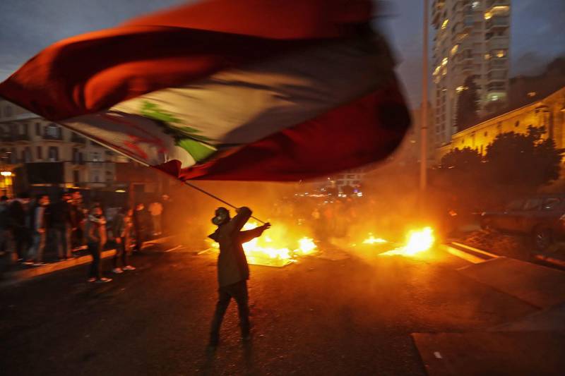 An anti-government protester waves the national flag in front of a burning barricade during ongoing demonstrations in Lebanon's capital Beirut. AFP