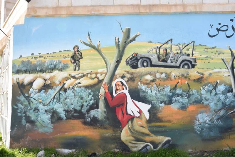 A mural of a Palestinian holding a vandalised tree, with the Israeli military in the background, in Beitin, West Bank. 