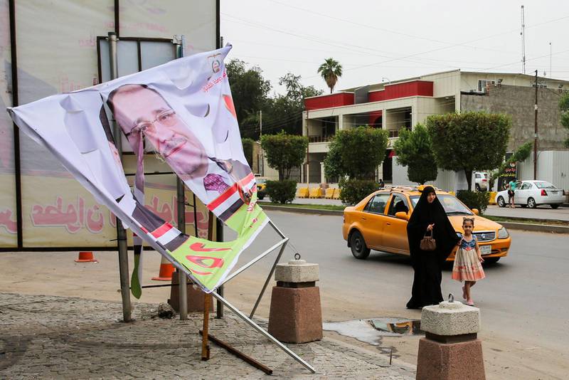 An Iraqi woman and a girl walk past an electoral banner for former Prime Minister Nuri al-Maliki that was damaged by a storm the day before, in the capital Baghdad on April 28, 2018.  / AFP PHOTO / SABAH ARAR