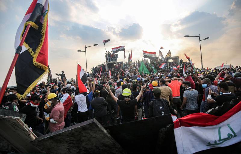 (FILES) In this file photo taken on October 29, 2019, Iraqi protesters wave national flags as they stand atop concrete barriers across the capital Baghdad's al-Jumhuriya bridge which connects between Tahrir Square and the high-security Green Zone, hosting government offices and foreign embassies, during the ongoing anti-government protests. In October 2019, unprecedented demonstrations across Iraq demanded the downfall of the ruling class. But after a year, a new government and nearly 600 protesters killed, virtually nothing has changed. / AFP / AHMAD AL-RUBAYE

