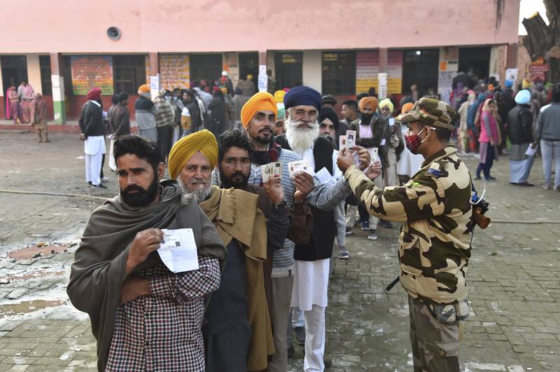 A paramilitary soldier checks identity cards of voters standing in a queue outside a polling station, at Attari village, about  45 kilometres (25 miles) from Amritsar, in the Indian state of Punjab, Sunday, Feb.  20, 2022.  (AP Photo / Prabhjot Gill)