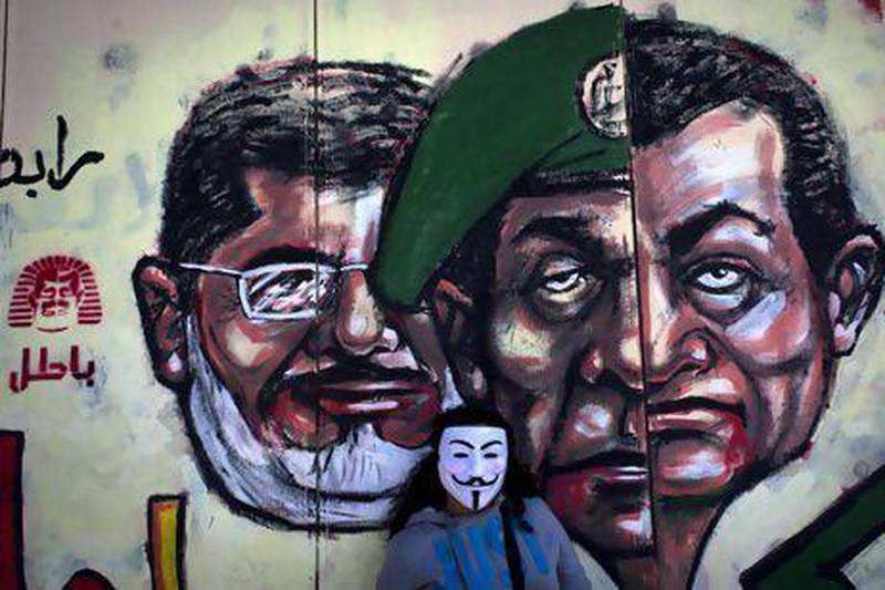 A protester wears a Guy Fawkes mask beside a mural painted on a wall of Cairo’s presidential palace depicting president Mohammed Morsi, left, former military council ruler Hussein Tantawi, centre, and ousted president Hosni Mubarak. It reads: ‘No, the Brotherhood's constitution is not valid’.