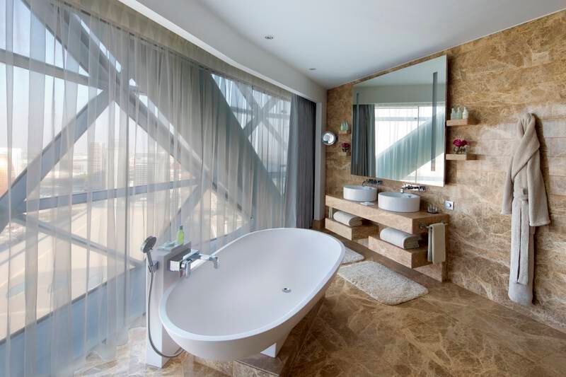 A large standalone bathtub overlooking the sea sits in a corner of the large bathroom