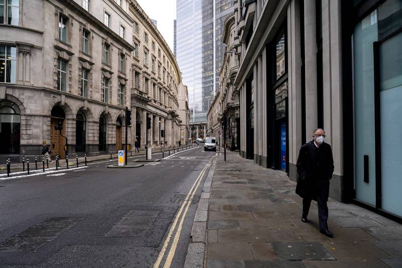 A man wears a face mask while walking in an empty street in the financial district, known as The City, in London. AP Photo