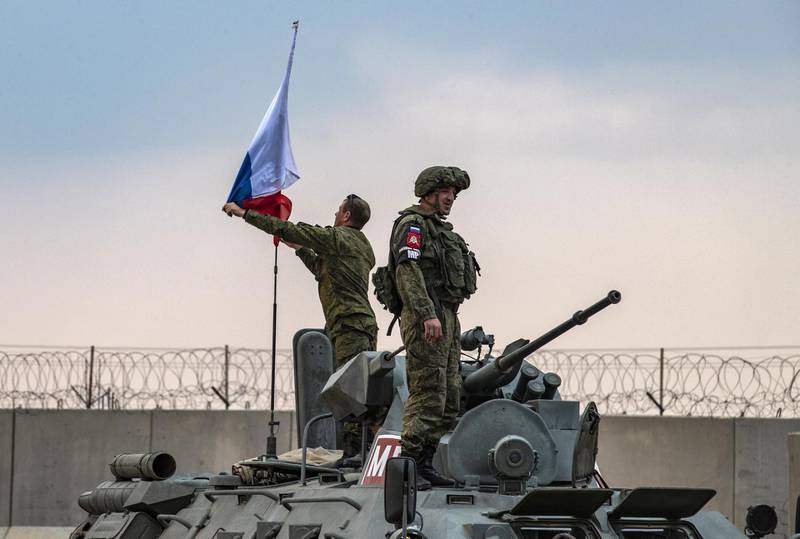 Russian troops on patrol with Turkish forces in the countryside of the town of Darbasiyah in Syria's northeastern Hasakeh province on the border with Turkey, raise a national flag atop an armoured personnel carrier on November 1, 2019. - Turkey started joint patrols with Russia in northern Syria today to verify whether Kurdish forces have withdrawn from a key border zone in compliance with a deal reached between the two governments. (Photo by Delil SOULEIMAN / AFP)