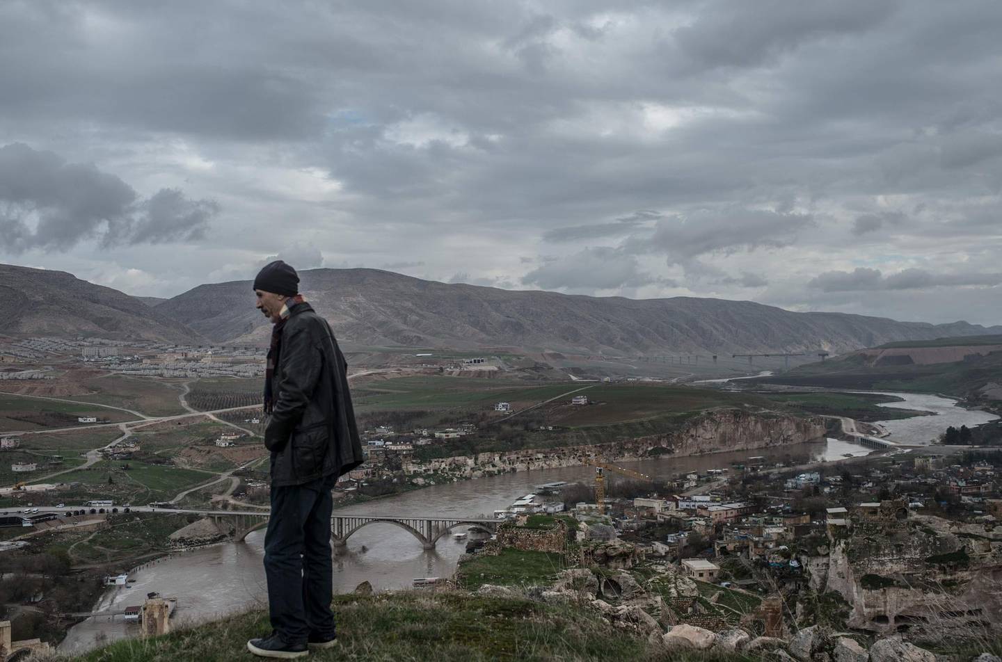 Ridvan Ayhan, a 58-year-old activist who fights against the Ilisi hydroelectric dam project, looks at the "new Hasankeyf" which is seen on the other side of Tigris river, on December 13, 2018, near the historical town of Hasankeyf in Turkey's Kurdish-majority southeast. The small town of Hasankeyf, inhabited for 12,000 years, is doomed to disappear in the months ahead under an artificial lake, as a result of the dam project. The dam will be Turkey's second largest and has been built downstream of the Tigris. / AFP / BULENT KILIC
