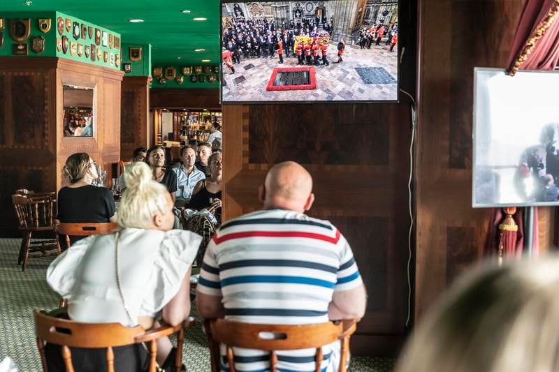 Mourners watch the funeral of Queen Elizabeth on television in the Golden Lion pub on board the QE2 in Port Rashid, Dubai. Antonie Robertson / The National
