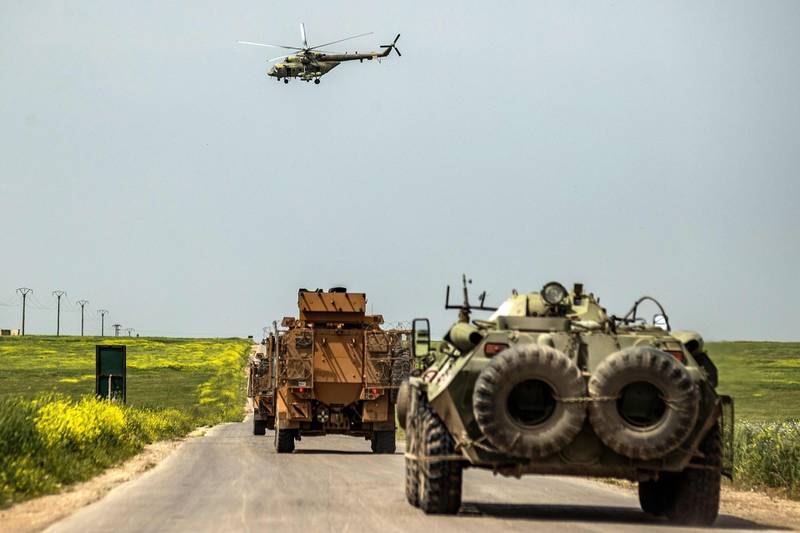 A Russian air force Mil Mi-28 military helicopter flies over Turkish (L) military MRAP (Mine-Resistant Ambush Protected) and Russian (R) armoured infantry vehicles (IFV) driving as part of a joint Turkish-Russian military patrol in the countryside of the Syrian town of Darbasiyah near the Turkish border in the northeastern province of Hasakah, on April 22, 2020.  / AFP / DELIL SOULEIMAN
