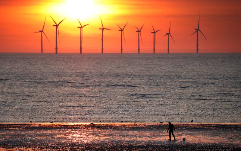 FILE PHOTO: A man stands on the beach as the sun sets behind the Burbo Bank wind farm near New Brighton, Britain, May 22, 2018. REUTERS/Phil Noble/File Photo