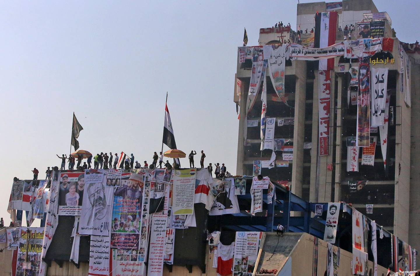 TOPSHOT - Iraqi protesters gather atop the abandoned "Turkish restaurant" building at Baghdad's Tahrir square during ongoing anti-government demonstrations on November 11, 2019. The United States has urged Iraq to hold early polls and carry out electoral reform, after a rights group warned a deadly crackdown on anti-government protesters could spiral into a "bloodbath". Three protesters were shot dead in the southern city of Nasiriyah on November 10 while dozens of demonstrators were wounded in Baghdad. / AFP / SABAH ARAR
