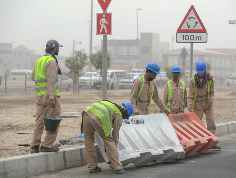 Road workers carry a barrier which was dragged by strong winds in the Musaffah area of Abu Dhabi. Victor Besa / The National