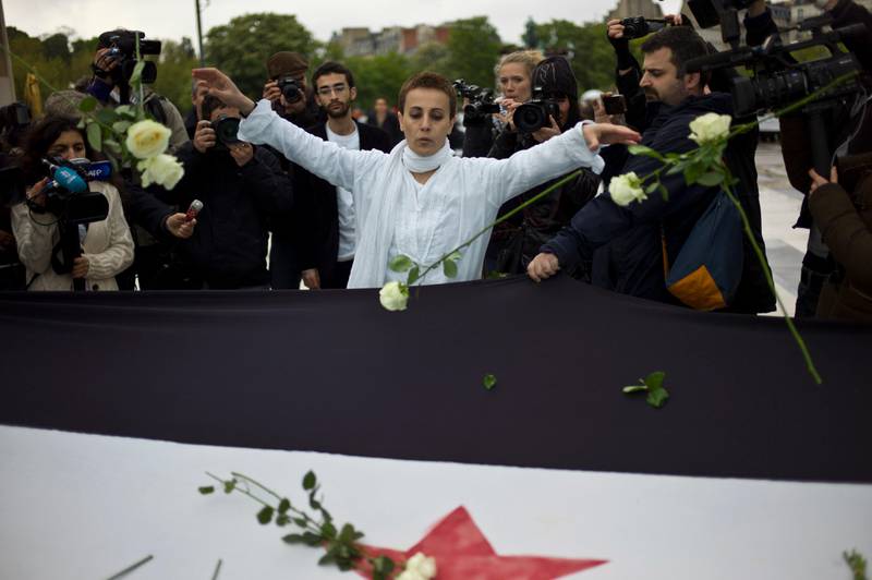 FILE - In this April 17, 2012 file photo, Syrian actress and activist, Fadwa Suleiman, center, throws roses on a giant Syrian flag during the 'White Wave' campaign to protest against the violence in Syria, in Paris. Syrian opposition groups said Thursday, Aug. 17, 2017 that Suleiman, an actress who took center stage at anti-government protests in the early days of the uprising against President Bashar Assad, has died. She was 46. Suleiman, who hails from Assad's minority Alawite sect, became a hero to many for taking a stand against his family's decades-old rule.(AP Photo/Thibault Camus, File)