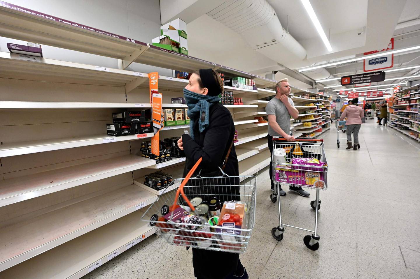 Shoppers are faced with partially empty shelves at a supermarket in London on March 14, 2020, as consumers worry about product shortages, leading to the stockpiling of household products due to the outbreak of the novel coronavirus COVID-19.   British Prime Minister Boris Johnson, who has faced criticism for his country's light touch approach to tackling the coronavirus outbreak, is preparing to review its approach and ban mass gatherings, according to government sources Saturday. / AFP / JUSTIN TALLIS
