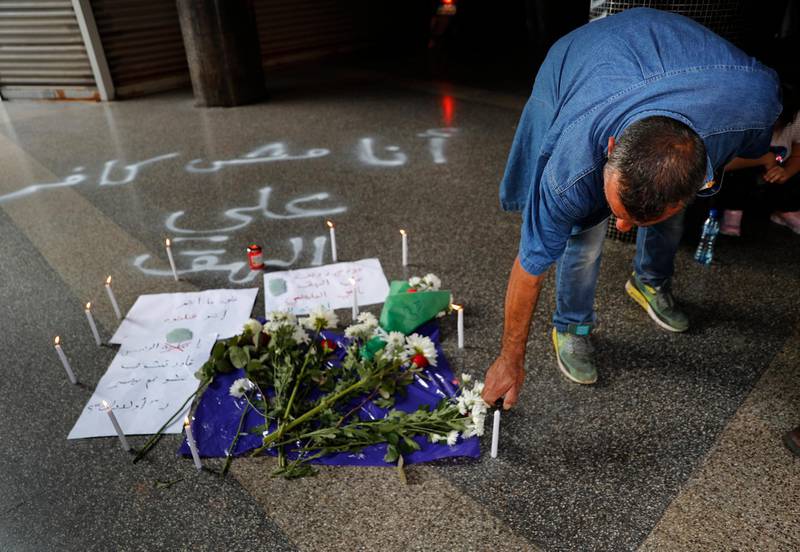 A man lights a candle at the scene where a Lebanese man killed himself on Beirut's commercial Hamra Street, apparently because of the deteriorating economic and financial crisis in the country, in Beirut, Lebanon, Friday, July 3, 2020. The man left a note that reads in Arabic: "I am not heretic but hunger is heresy," words taken from a Lebanese song. Security officials said they were investigating the incident and motives for his suicide. The Arabic words sprayed on the ground by protesters read:"I am not heretic but hunger is heresy and the name of the killed man Ali al-Hok." (AP Photo/Hussein Malla)