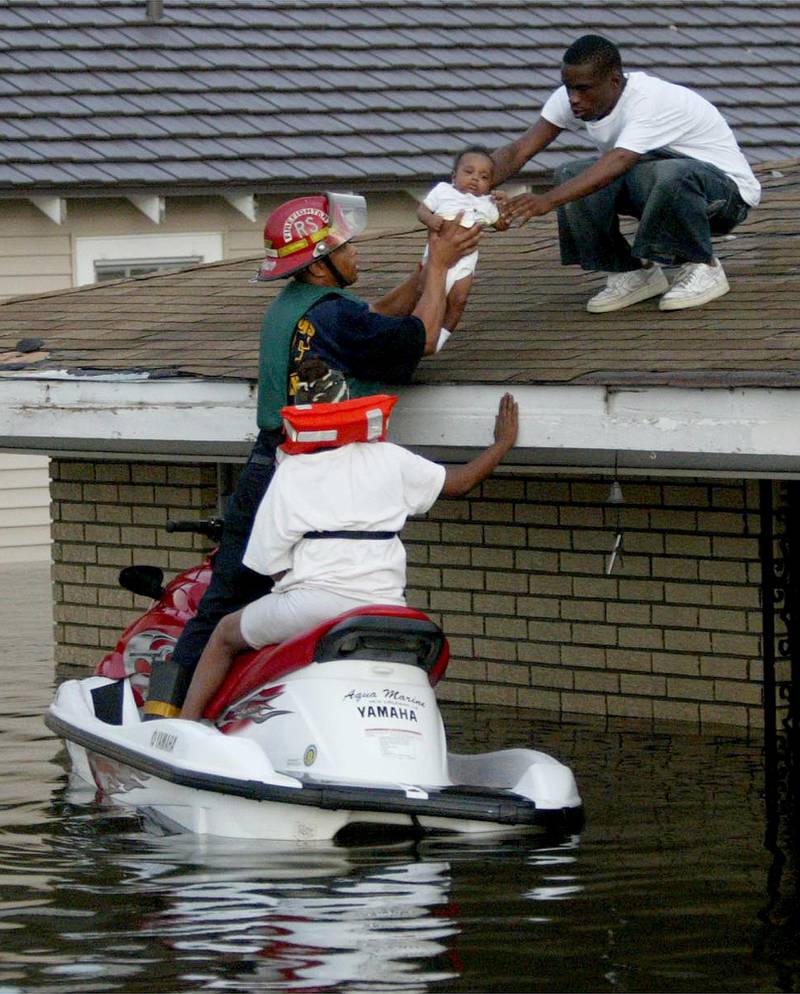 FILE - In this Monday, Aug. 29, 2005 file photo, Marshall Martin, on roof, hands 3-month-old Christopher Collins to New Orleans Fire and Rescue officer Jonathan Pajeaud while the child's grandmother, Sheila Martin, waits on a water craft during evacuations in the 7th Ward of New Orleans, following the passage of Hurricane Katrina through the area. (Gary Coronado/Palm Beach Post via AP)