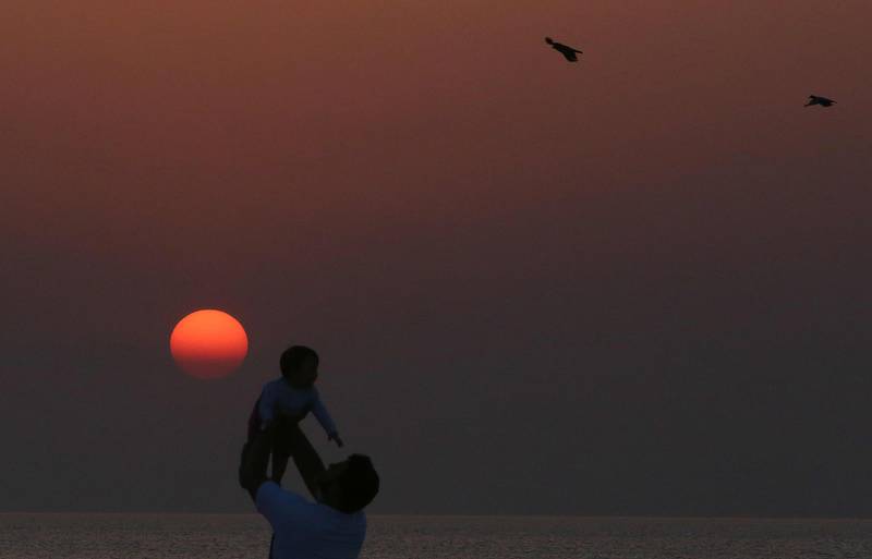 A man tosses a baby against the red sunrise as birds fly past on the beach in Kuwait City on the last day of the Eid al-Fitr holiday.  AFP