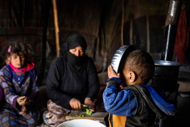 A Syrian woman prepares food with two children at the Kabsh camp for the displaced people in the countryside near Syria's northern city of Raqa during the Muslim holy month of Ramadan on April 7, 2022.  (Photo by Delil souleiman  /  AFP)