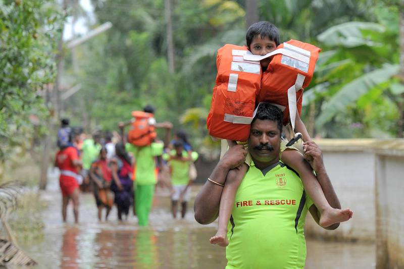 Kerala and Tamil Nadu Fire Force personnel carry children on their shoulders through flood waters during a rescue operation in Annamanada village in Thrissur District, Kerala. AFP