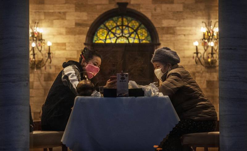 Chinese women wear protective masks as they eat dinner at an open restaurant in Beijing, China.  Getty
