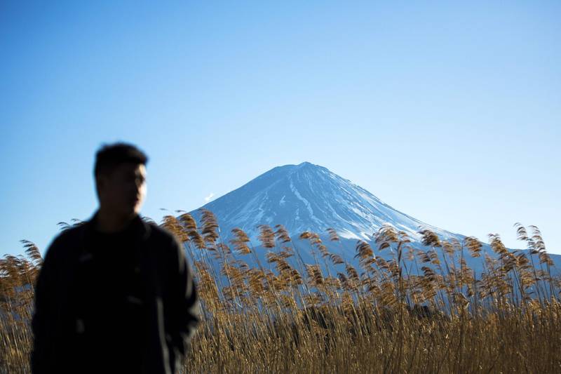 TOPSHOT - In this picture taken on January 2, 2018, a tourist stands by Lake Kawaguchi overlooking Mount Fuji in the town of Fujikawaguchiko, Yamanashi prefecture. / AFP PHOTO / Behrouz MEHRI