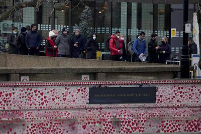 People queue alongside the National Covid Memorial Wall as they await coronavirus booster vaccinations at St Thomas' Hospital,  in London. AP Photo