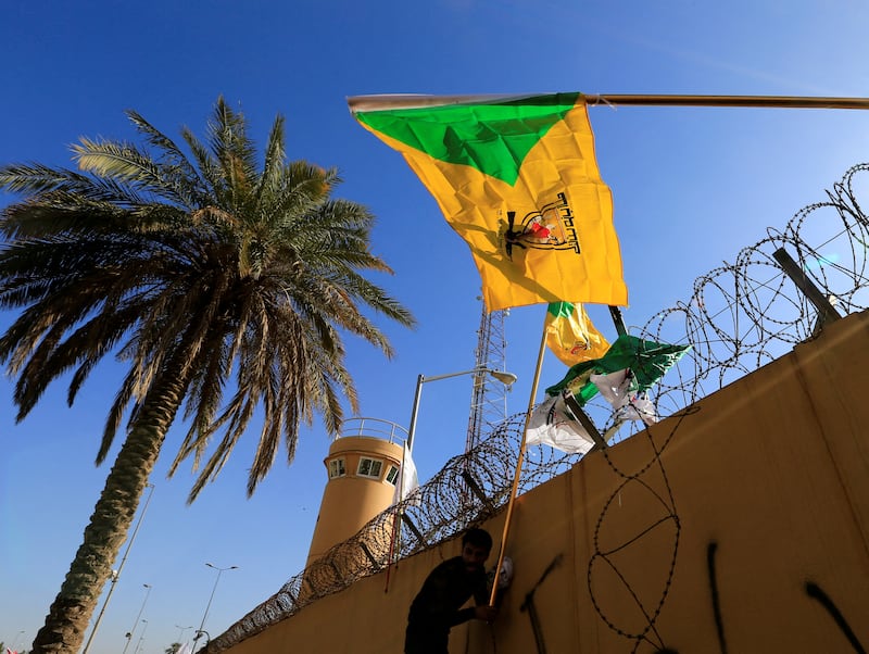 The flag of the Kataib Hezbollah militia group is raised during a protest outside the US Embassy in Baghdad in December 2019. Reuters