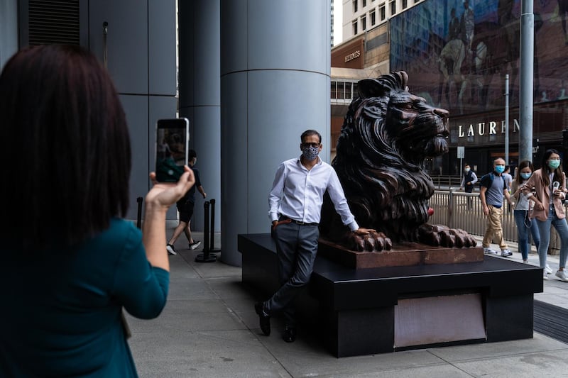 A person stands for a photograph next to a statue of a lion in front of the HSBC Holdings Plc headquarters building in Hong Kong. Bloomberg