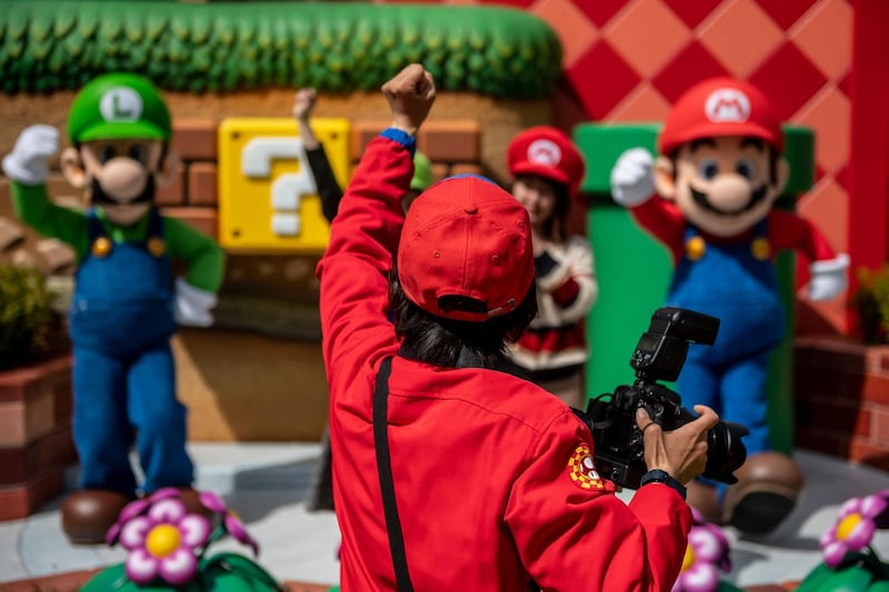 A staff member (front) rousing fans for posed photographs with Super Mario Bros characters Mario, right, and Luigi, left. AFP