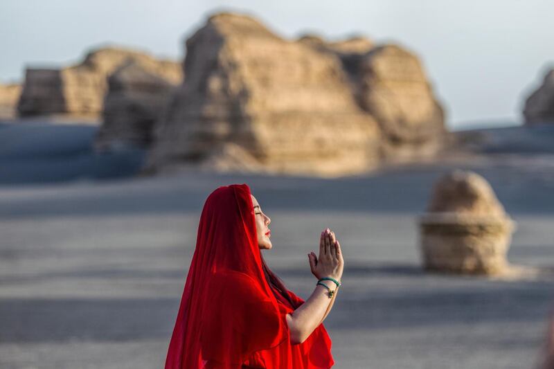 A woman prays towards the sun in the desert in Yardang Geopark.