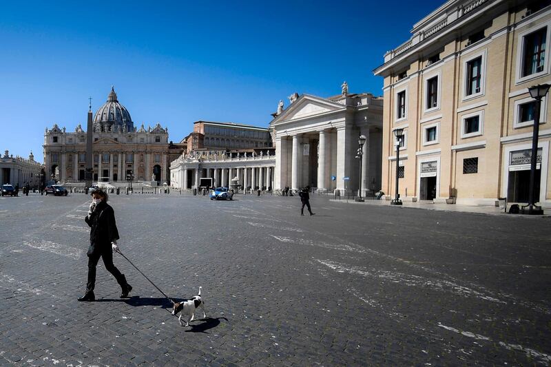 A woman wearing a face mask walks her dog along the border between Italy and The Vatican on March 25, 2020 in Rome during the lockdown following the COVID-19 new coronavirus pandemic.  / AFP / Filippo MONTEFORTE
