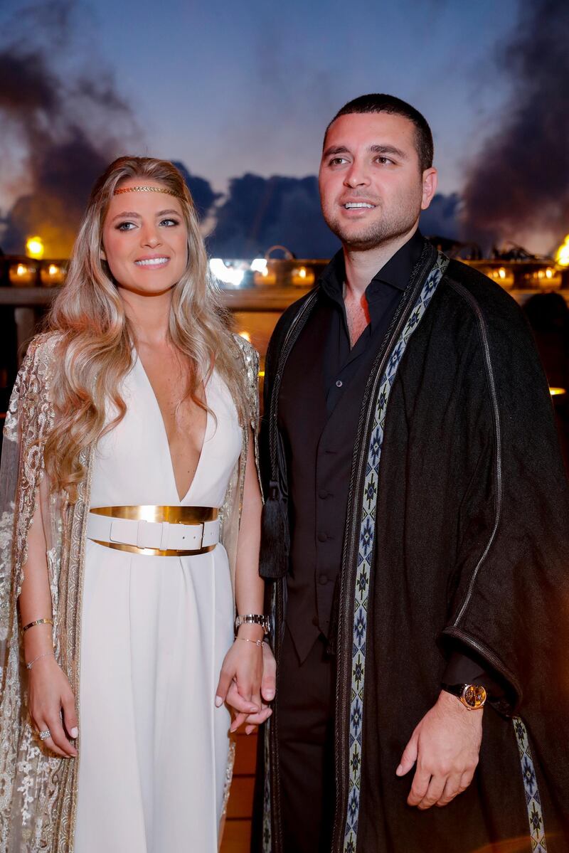 The couple at the pre-party the night before at Plateau de Bakish. Christina is in a cream jumpsuit with a gold cape from the Haute Couture Fall-Winter 2019/2020 collection.