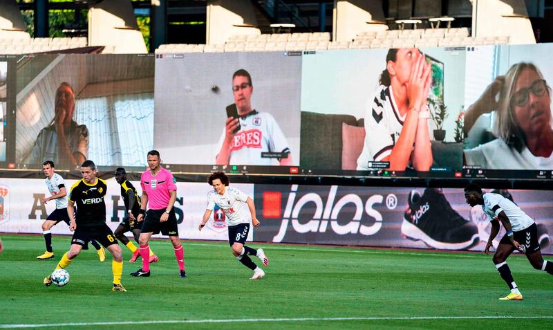 Players vie for the ball as fans are streamed live on to the screens on the sidelines during the 3F Super League football match between AGF and Randers FC. AFP